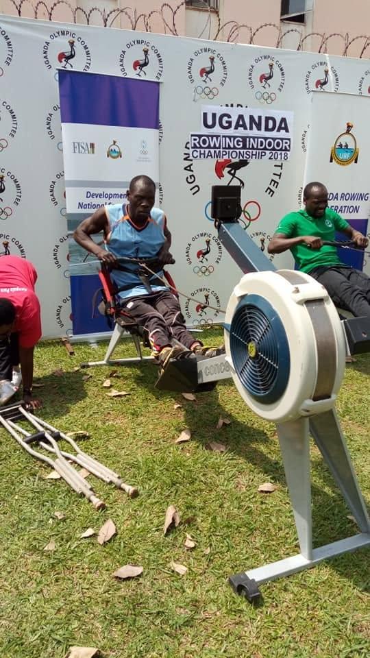 An athlete trains on an ergometer beside a Uganda Para-Rowing banner.