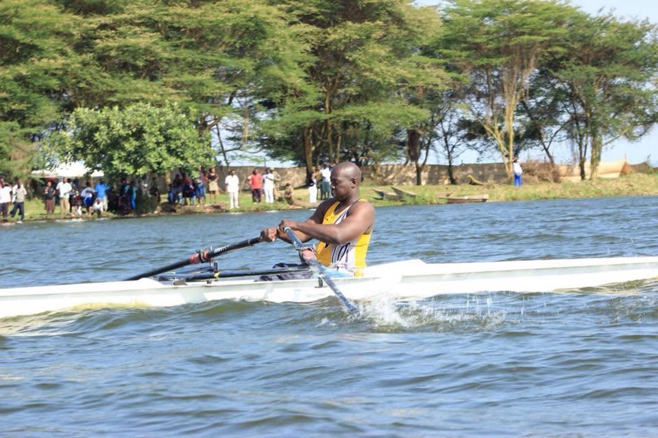 A Para rowing athlete mid-stroke on open water, oars driving through a burst of spray.