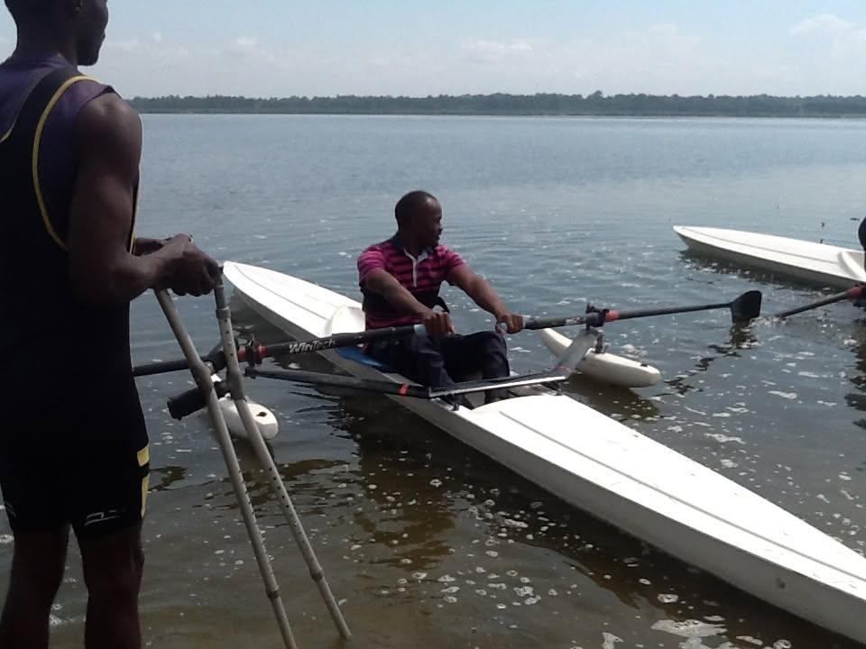 A coach helps an athlete into a boat among water hyacinth.