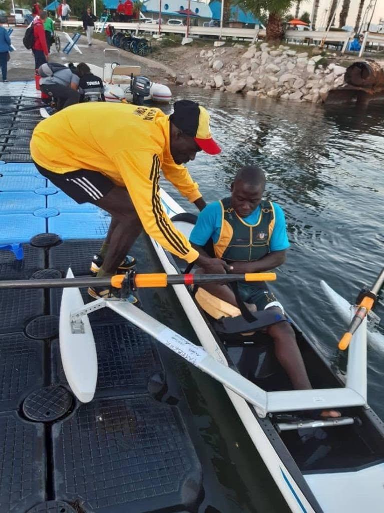 Athletes load a boat at the water's edge.