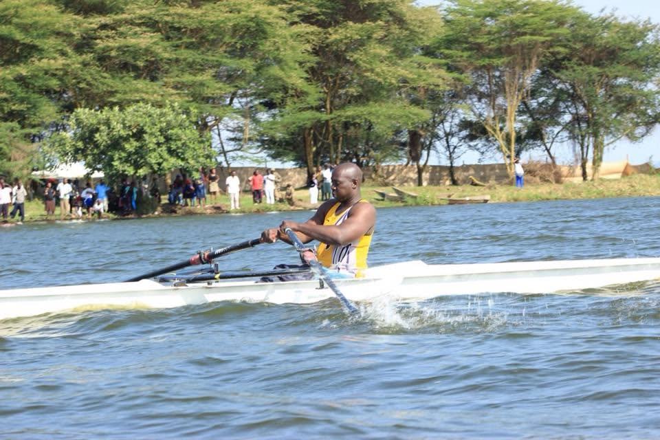 A Para rowing athlete mid-stroke on open water in Uganda, oars driving through a burst of spray.