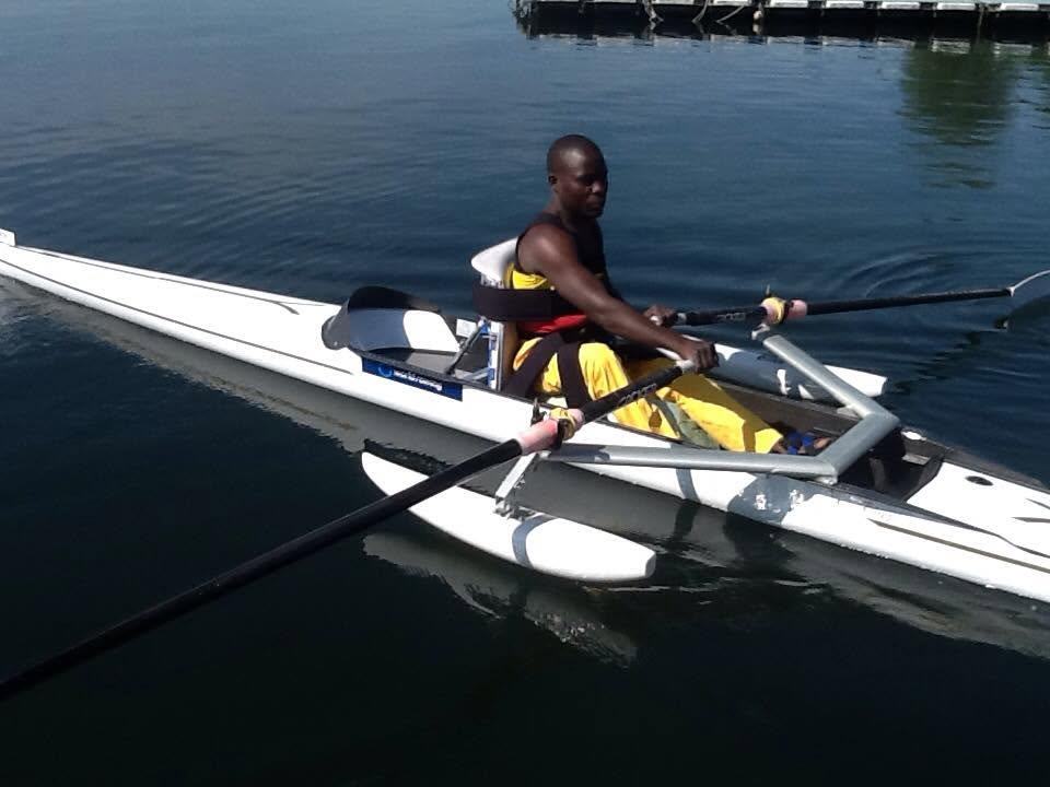 An athlete rowing an adapted single scull across calm water near the boathouse.